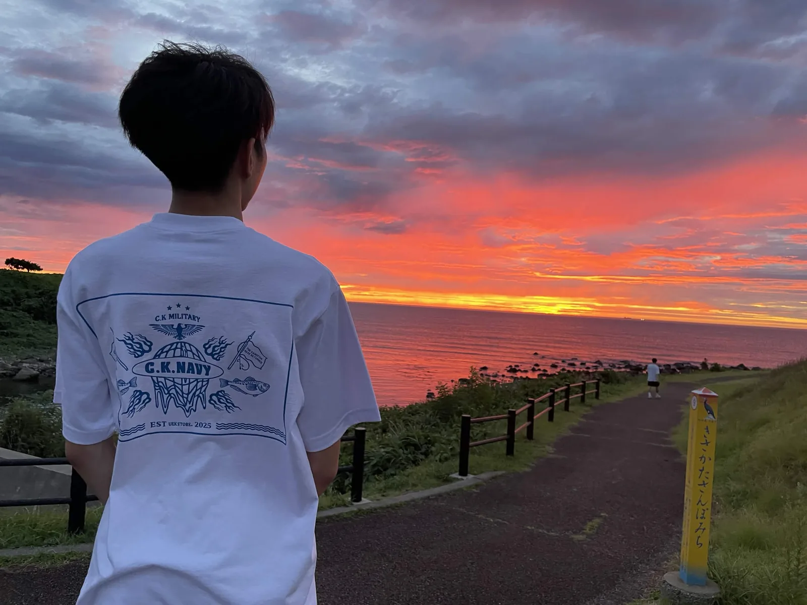 UEK STOREのTシャツを着て、秋田の海に沈む夕日を眺める片岡